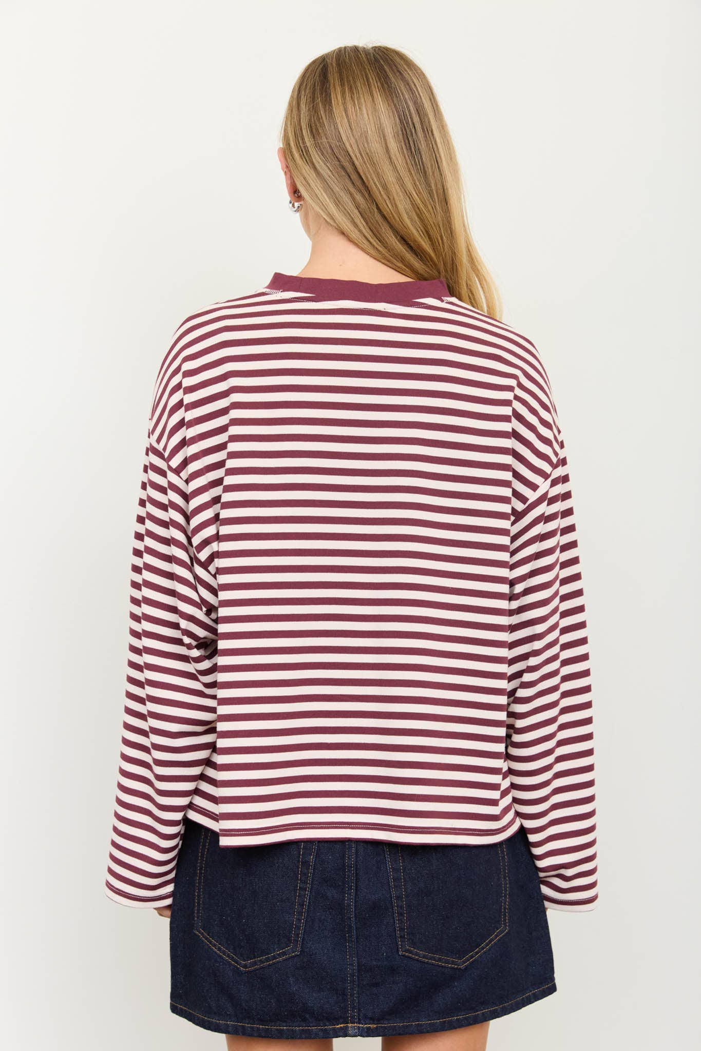 A woman viewed from the back wearing a long-sleeve striped top with dark red and white horizontal stripes, paired with a dark denim skirt, against a plain white background.