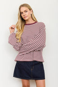 A blonde woman modeling a long-sleeve top with horizontal burgundy and white stripes, paired with a dark denim mini skirt, against a plain white background.