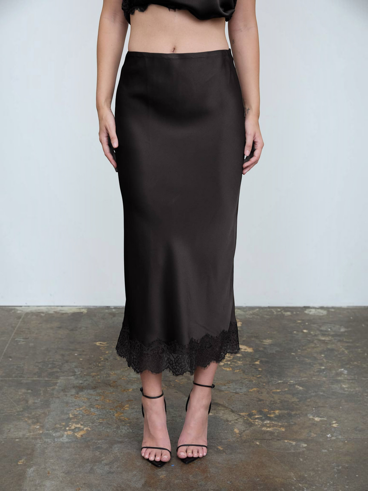 Mialur black satin midi skirt with delicate lace trim hem and high-waisted silhouette worn with black heels