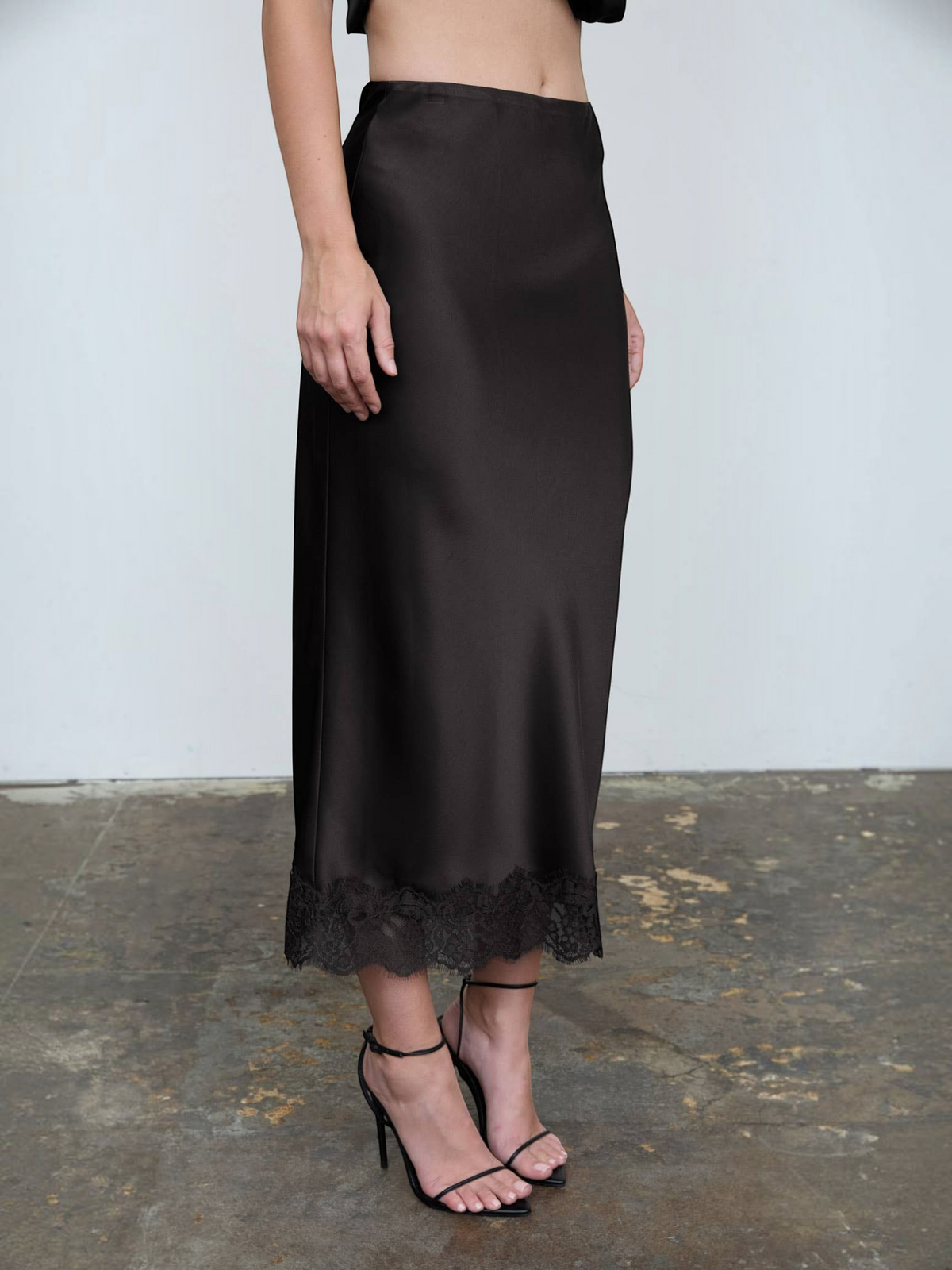 Mialur black satin midi skirt featuring a delicate lace hem and high-waisted silhouette worn with black heels.