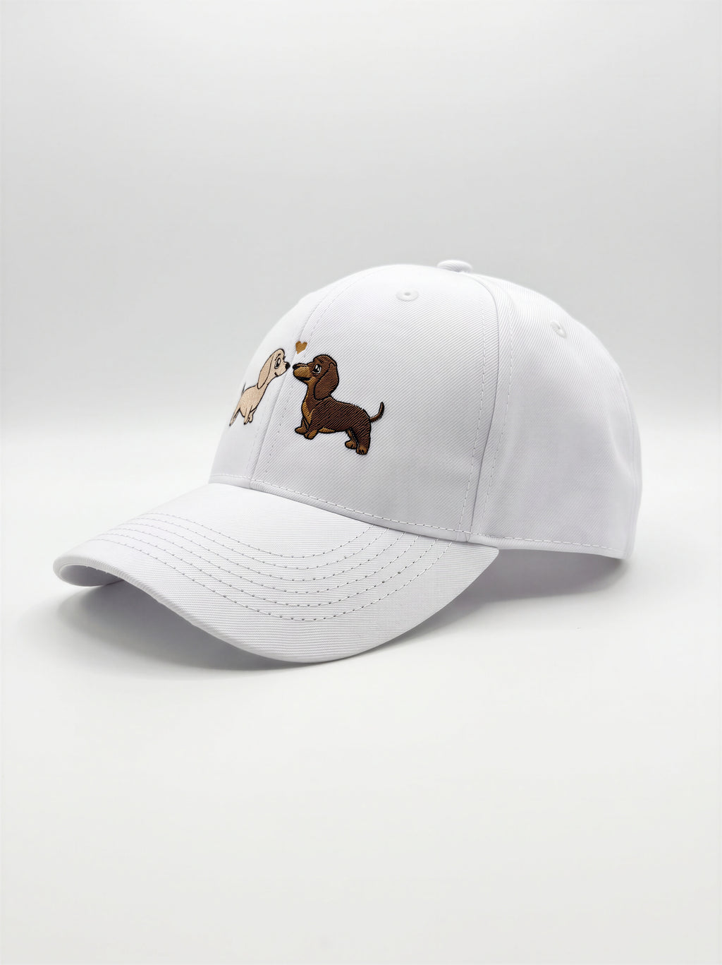 Mialur Boutique - A white baseball cap featuring embroidered cartoon dachshund dogs on the front panels, set against a seamless light gray studio background.