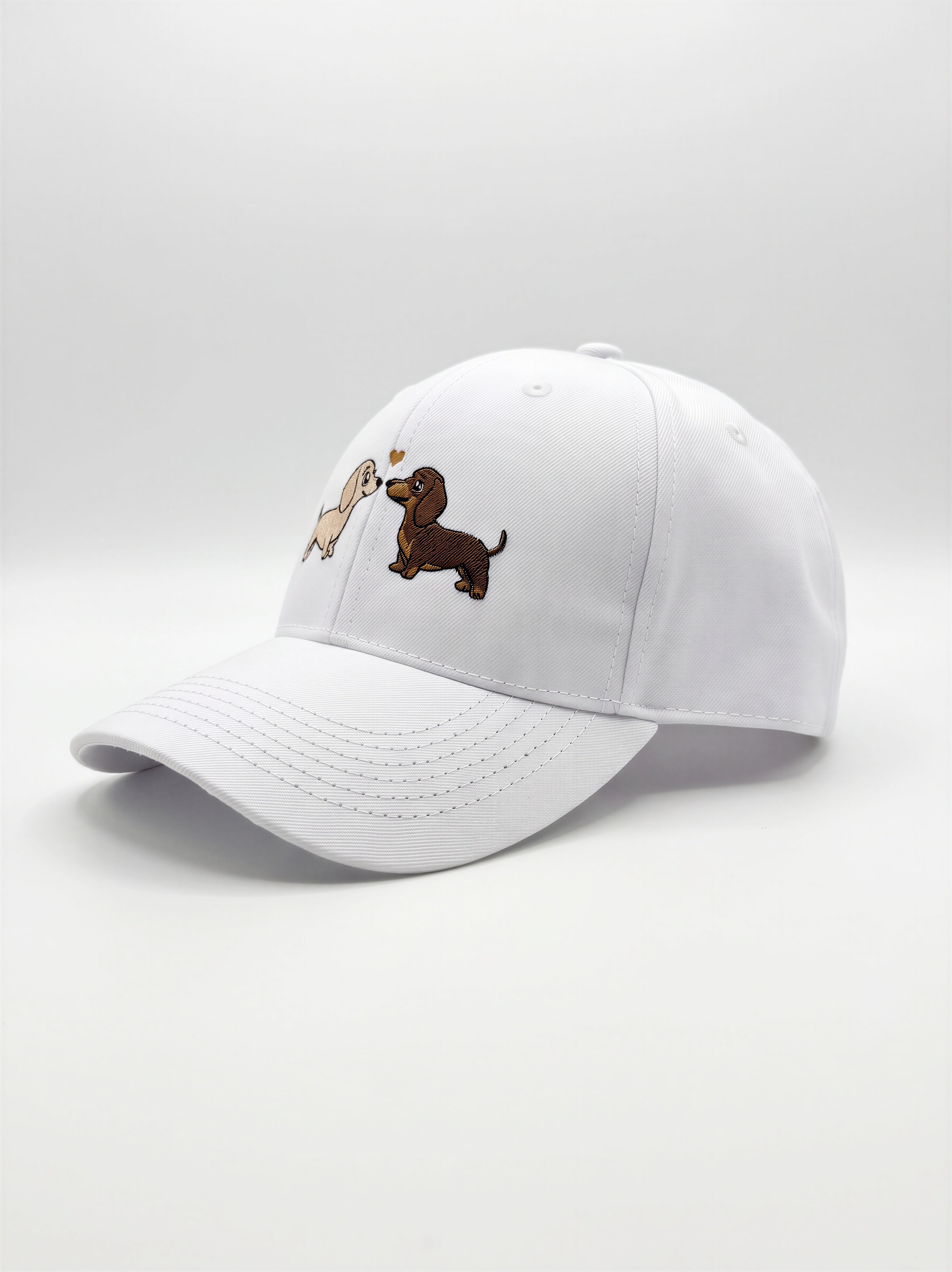 Mialur Boutique - A white baseball cap featuring embroidered cartoon dachshund dogs on the front panels, set against a seamless light gray studio background.