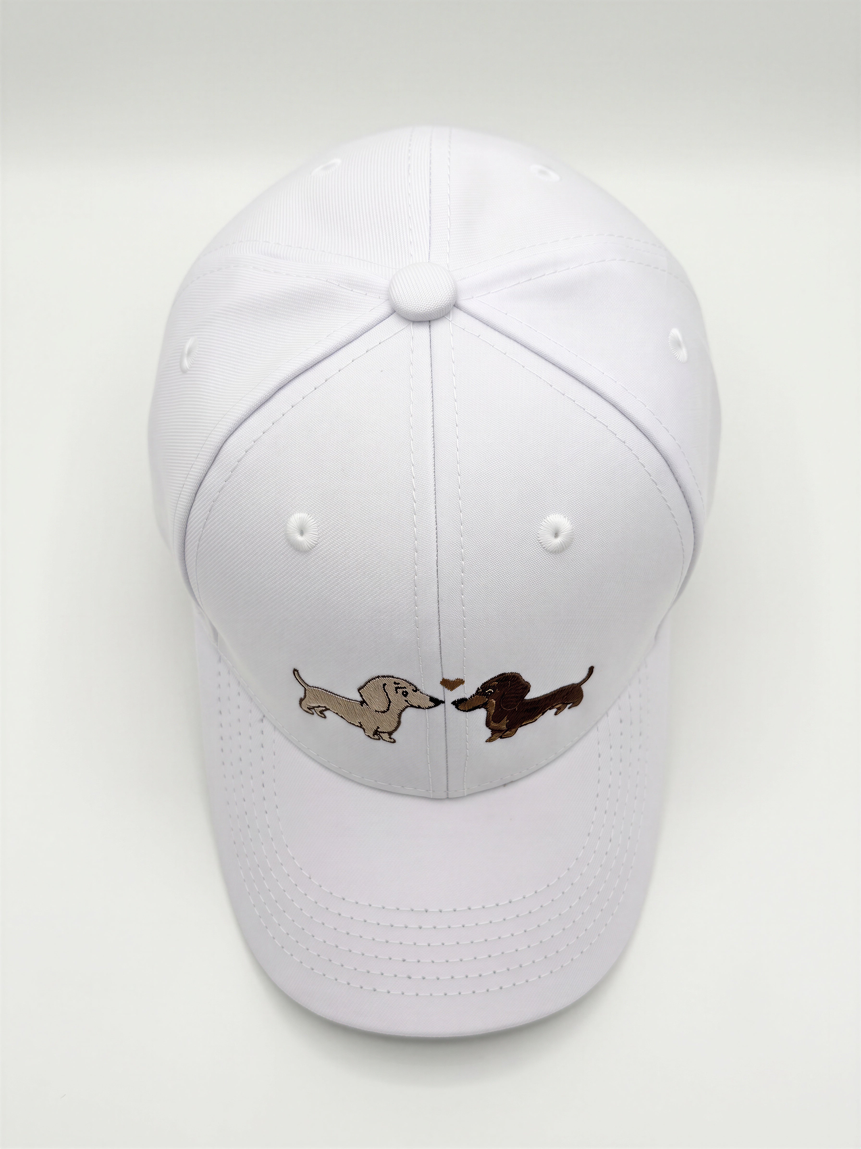 Mialur Boutique - A white baseball cap featuring an embroidered design of two dachshunds facing each other with a small heart between them, set against a plain light gray background.