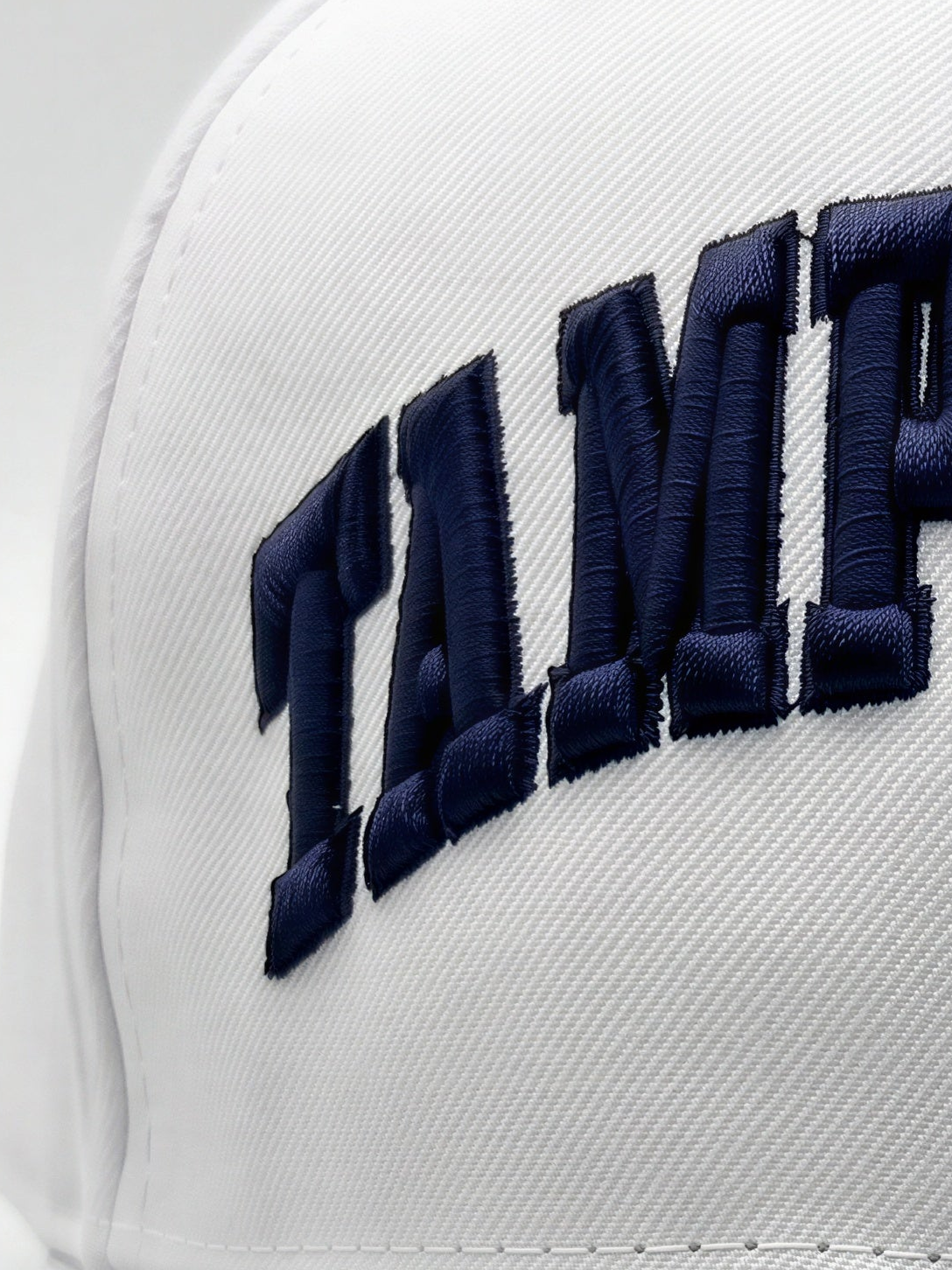 Close-up of a white structured cap with large navy blue embroidered lettering on the front panel.
