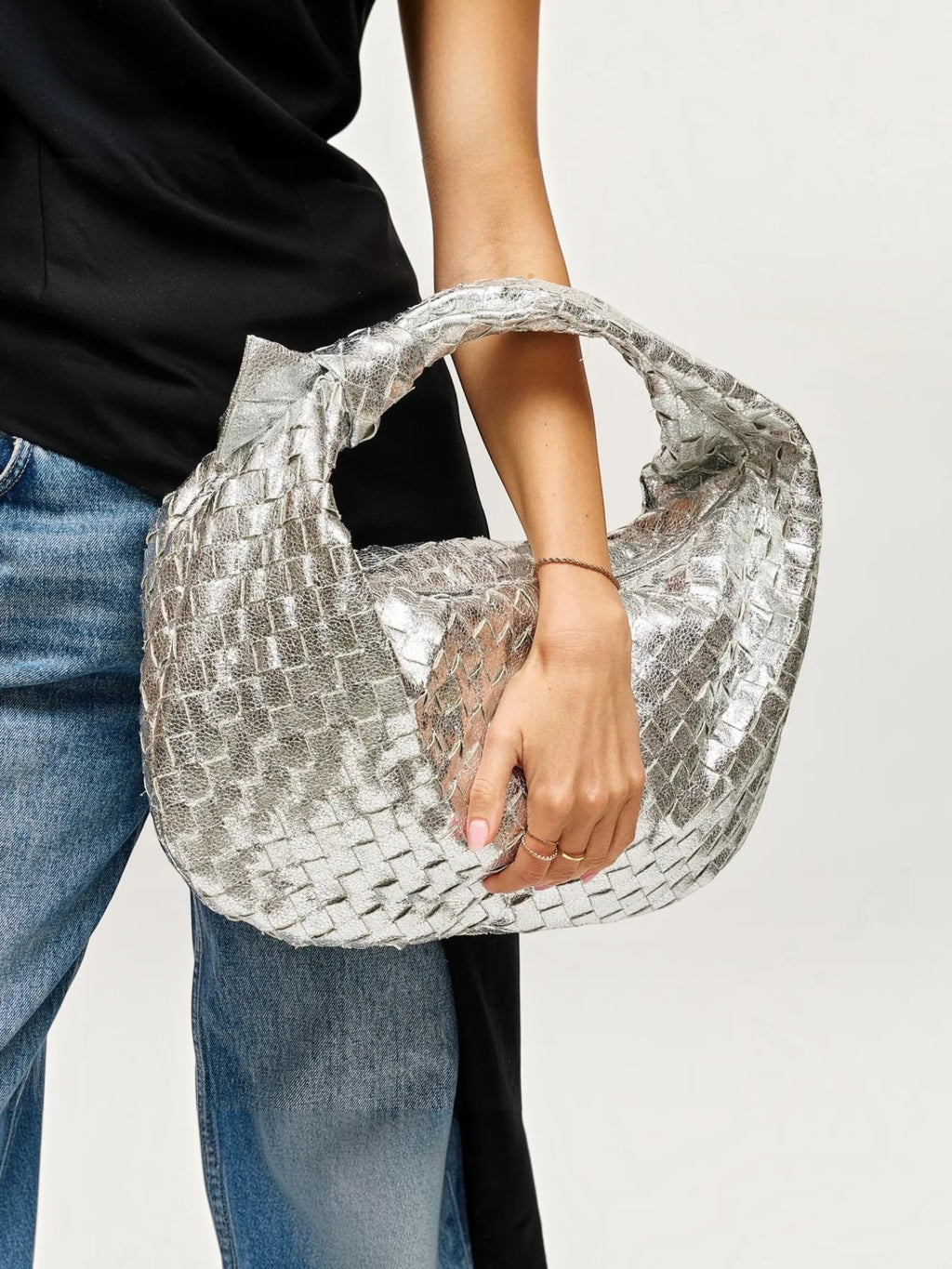 Mialur Aspen Bag in metallic silver with a slouchy woven texture held by a model wearing a black top and blue jeans.