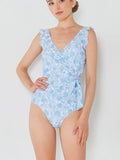 Model wearing Mialur Santorini blue and white floral print one-piece swimsuit with ruffle straps and wrap silhouette.