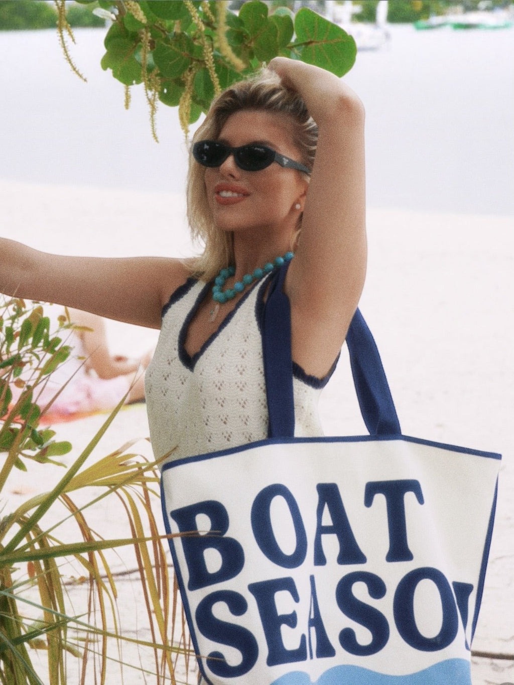 Mialur Boat Season ivory cotton canvas tote bag with blue lettering and wave graphic held by a woman on a beach