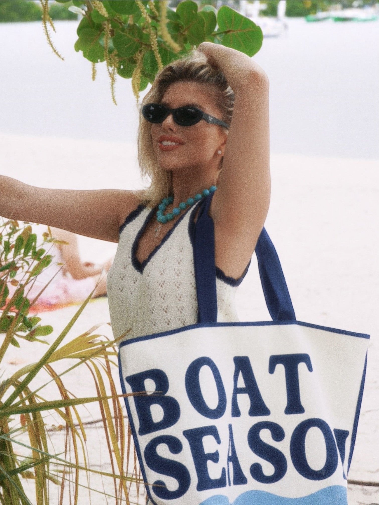 Mialur Boat Season ivory cotton canvas tote bag with blue lettering and wave graphic held by a woman on a beach
