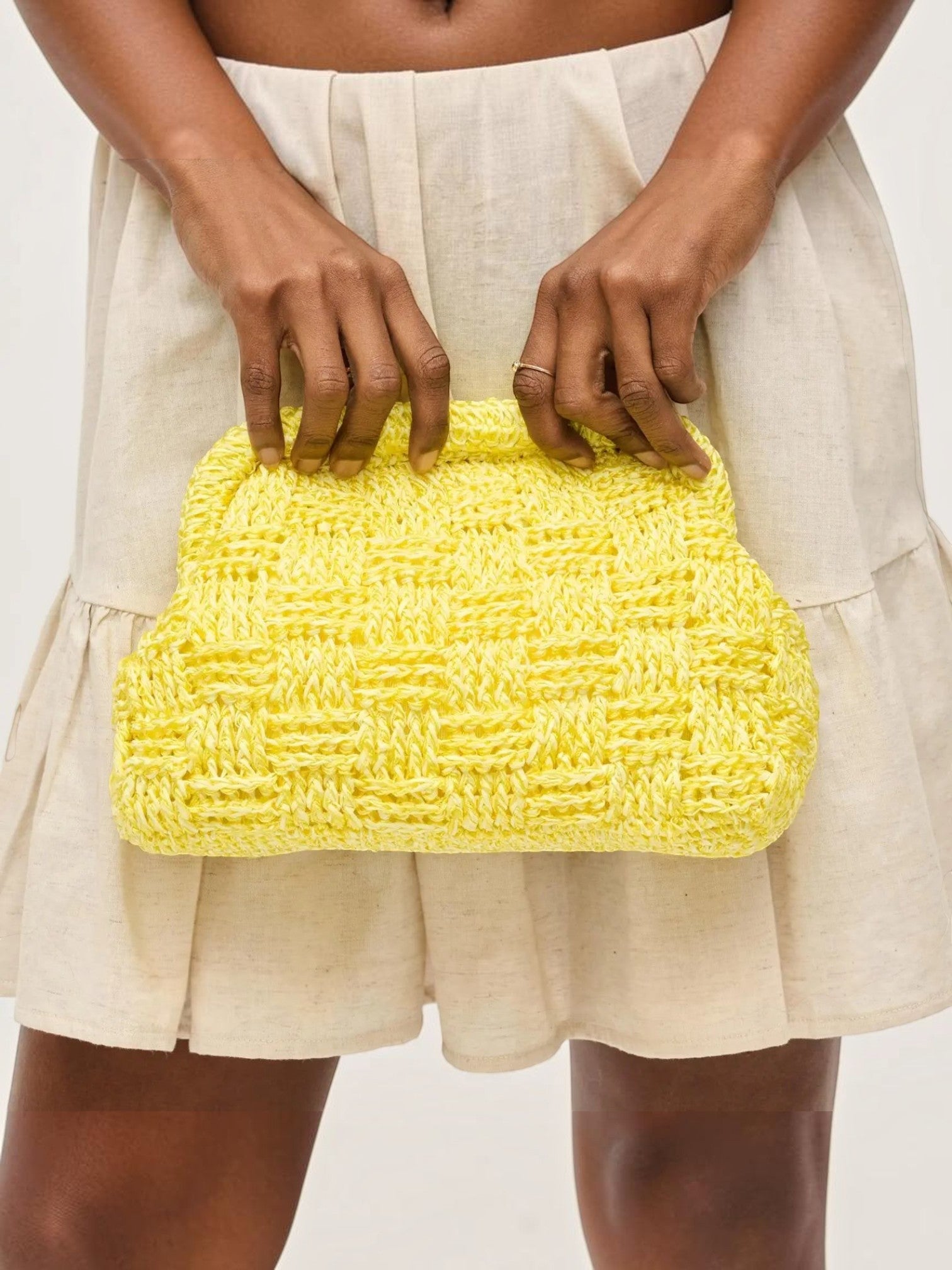 Mialur Butter Woven Clutch in bright yellow with a textured finish held by a model wearing a beige linen dress.