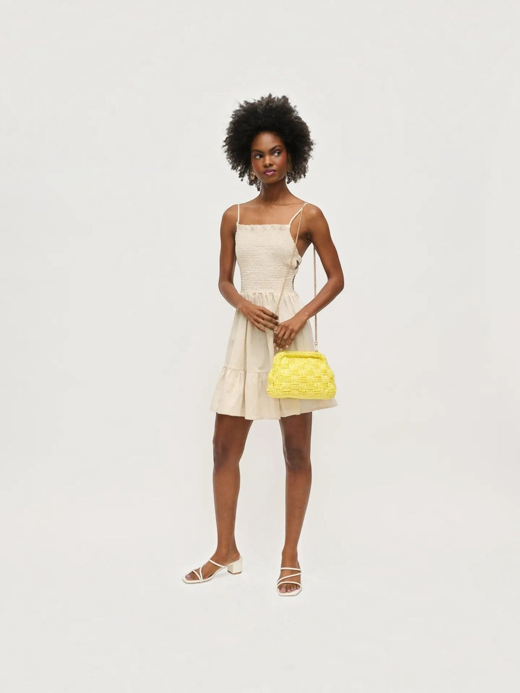 Model wearing a Mialur butter yellow woven clutch with gold chain strap and a beige sundress against a white background