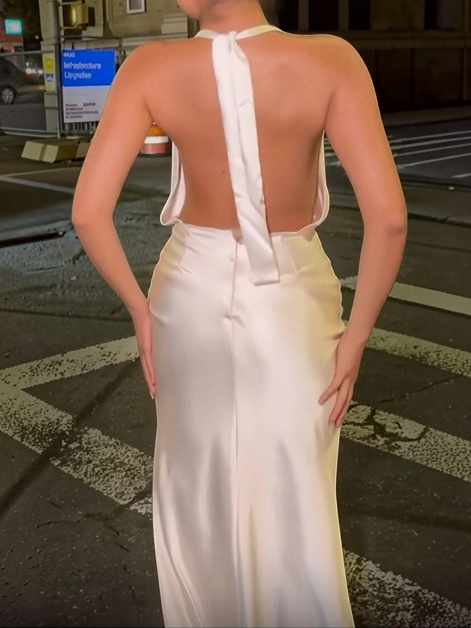 Back view of a woman wearing a Mialur champagne satin maxi dress with a cowl neckline and halter straps.