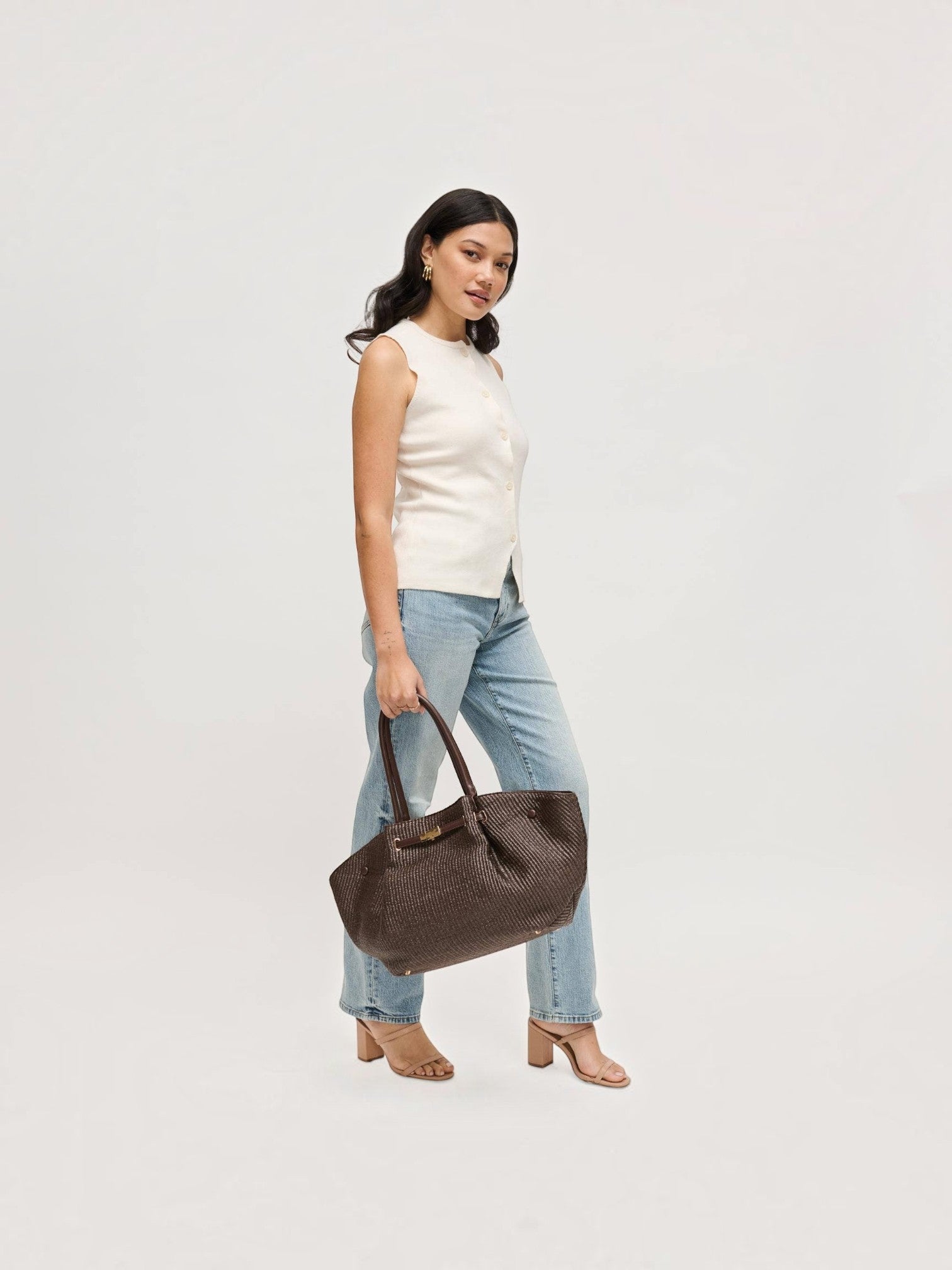 Mialur model carrying a chocolate brown woven tote bag with gold-tone hardware, styled with a white top and jeans.