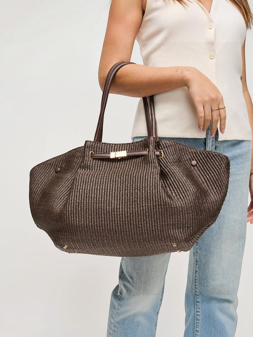 Mialur chocolate brown woven tote bag with gold-tone hardware and shoulder straps, held by a woman in casual attire.