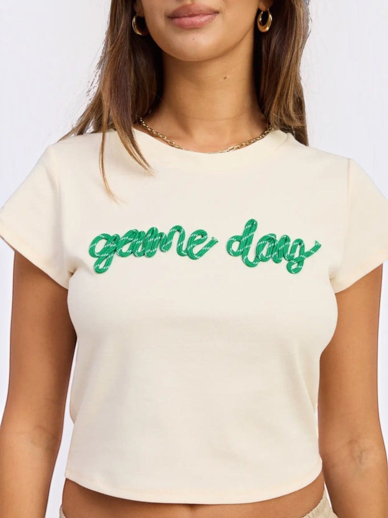 Mialur cream fitted baby tee with green game day script text for football season, worn by a woman.