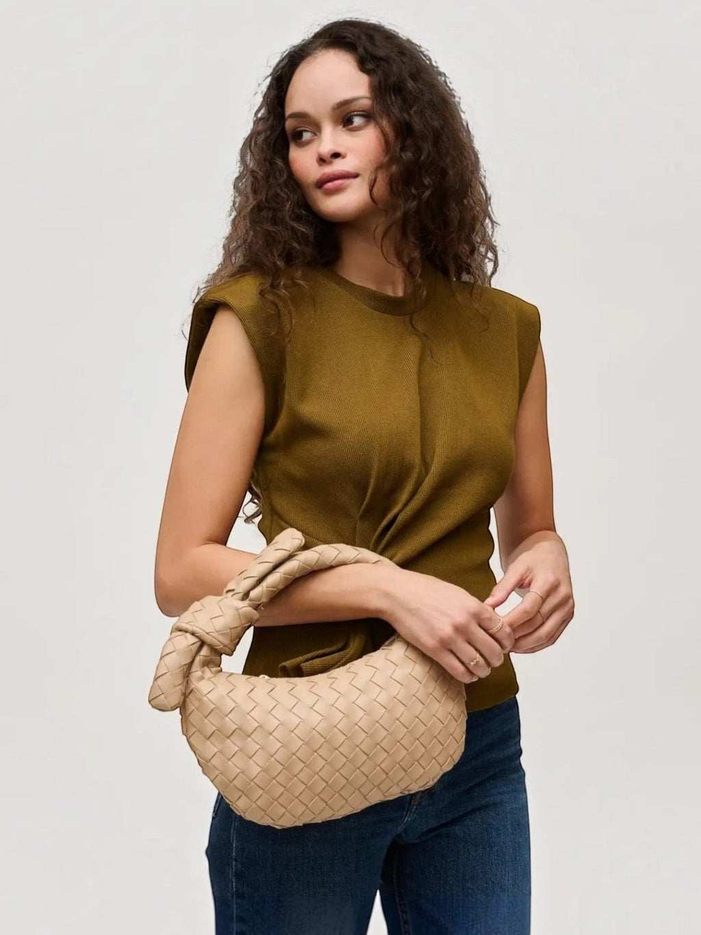 Model holding a Mialur tan woven vegan leather Emery Clutch with a signature knot handle against a neutral background.