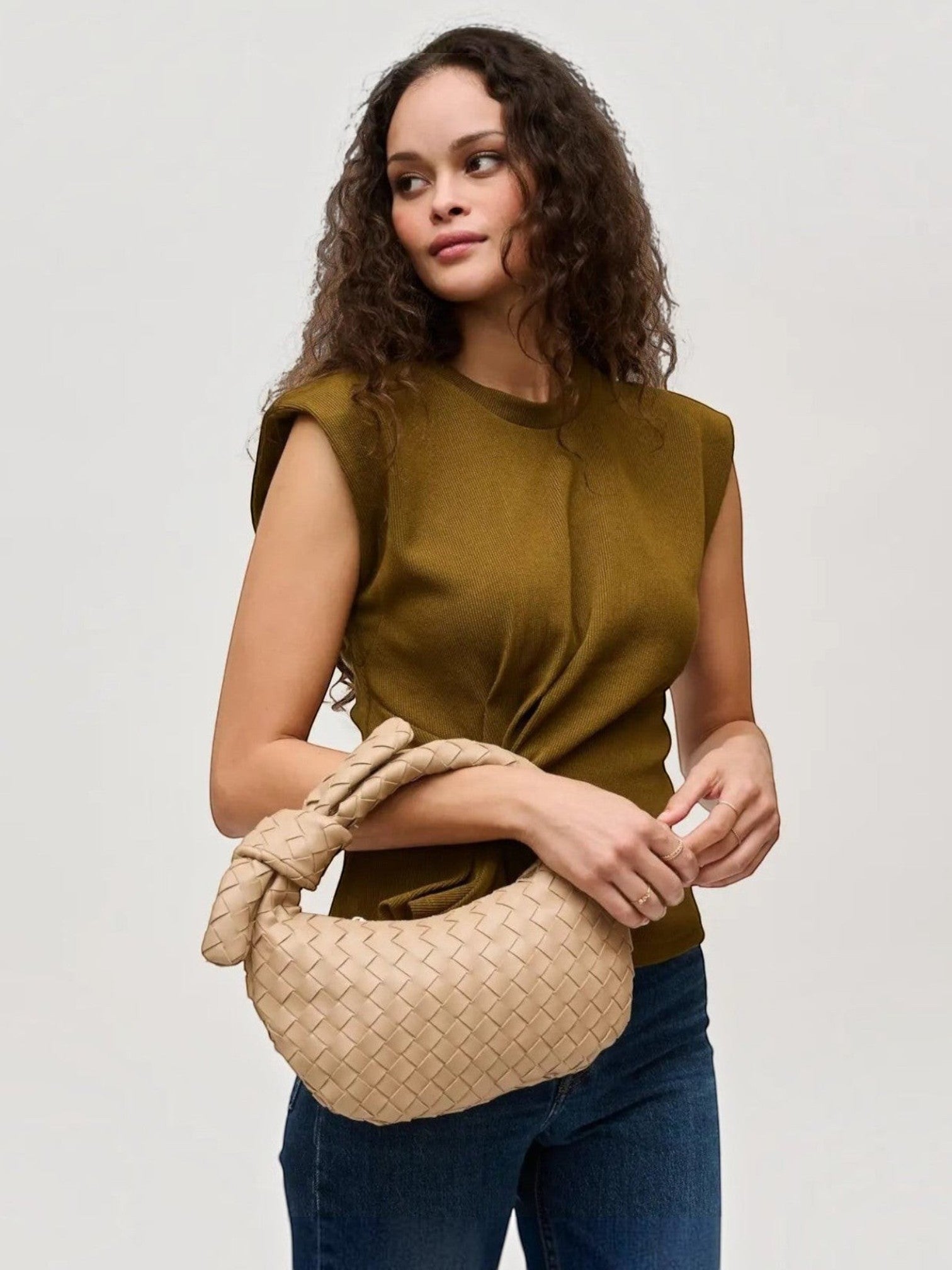 Model holding a Mialur tan woven vegan leather Emery Clutch with a signature knot handle against a neutral background.