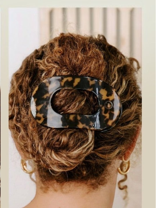 Mialur Boutique - A close-up back view of a person with curly brown hair styled in a low bun, secured with a glossy tortoiseshell hair claw clip. The clip has a black, brown, and tan leopard pattern.