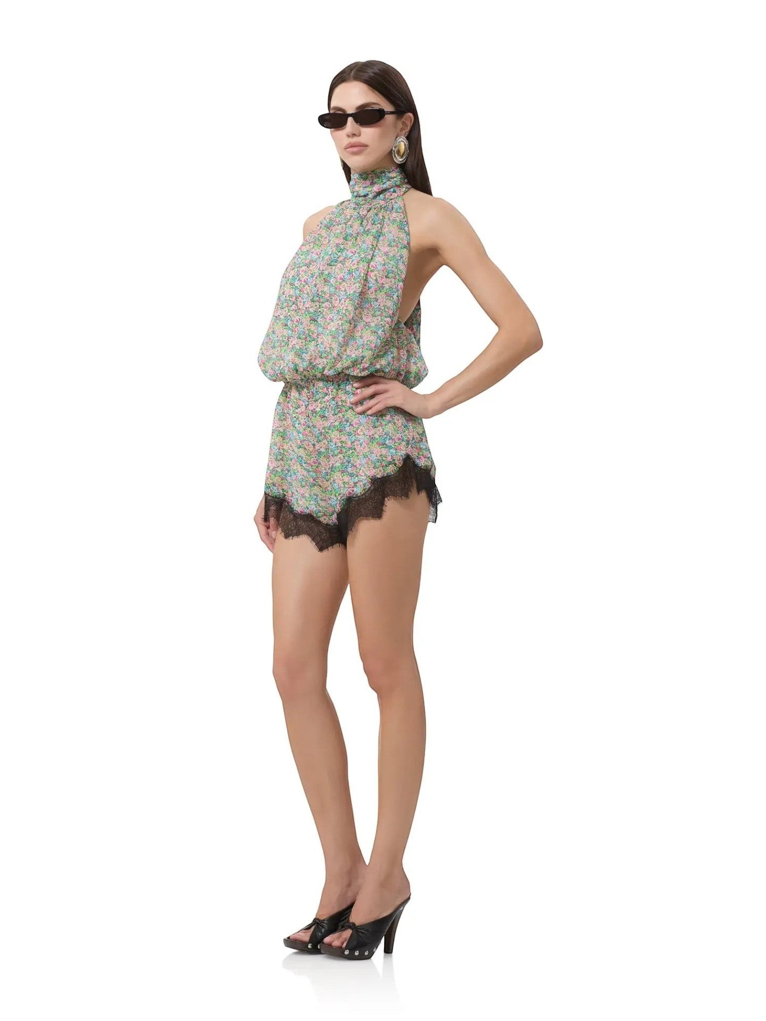 Model wearing Mialur Fleur floral romper with high neckline and black lace hem, styled with sunglasses and heels.