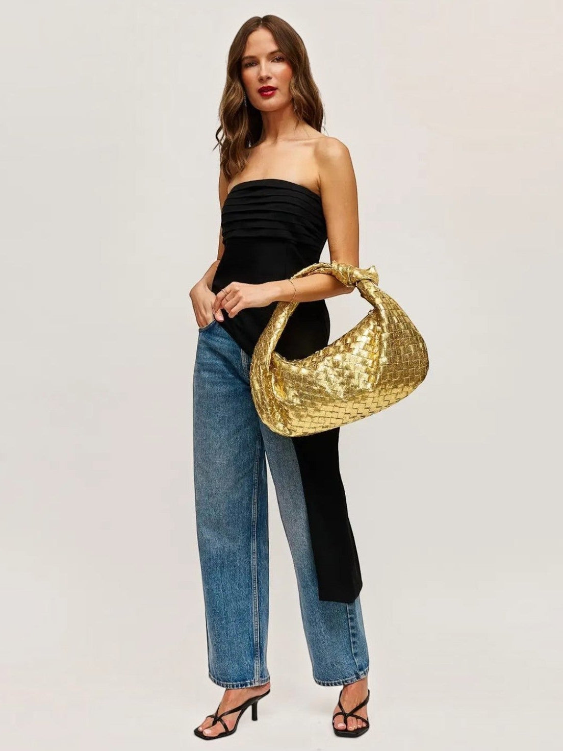 Model wearing a Mialur gold woven hobo bag with a black strapless top and blue jeans against a neutral background.
