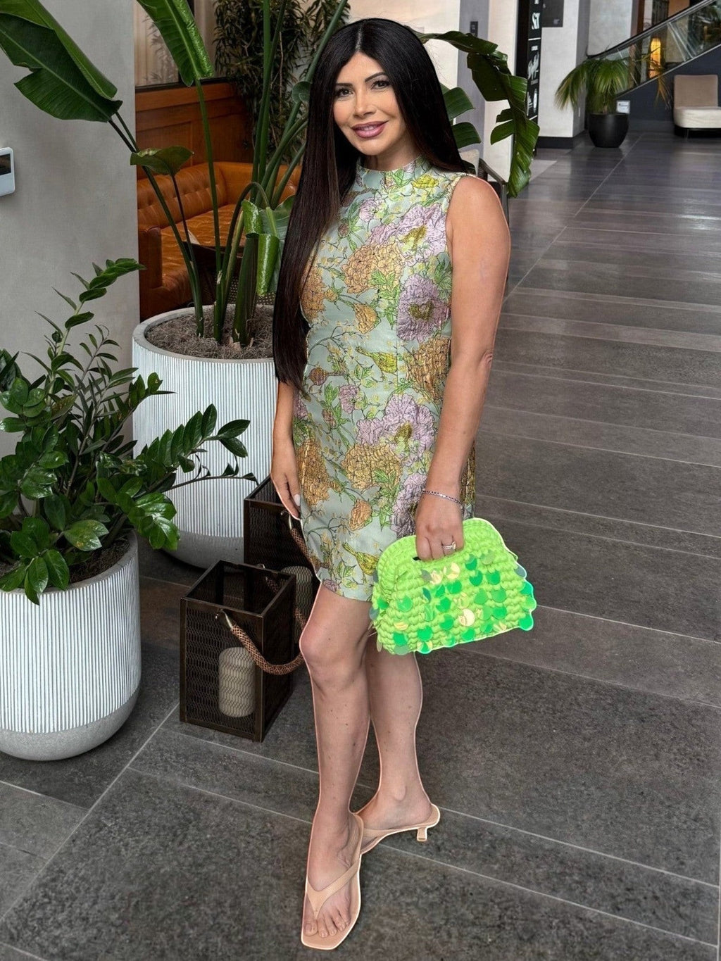 Woman holding a Mialur green woven handbag with iridescent paillettes, styled with a floral dress and sandals.