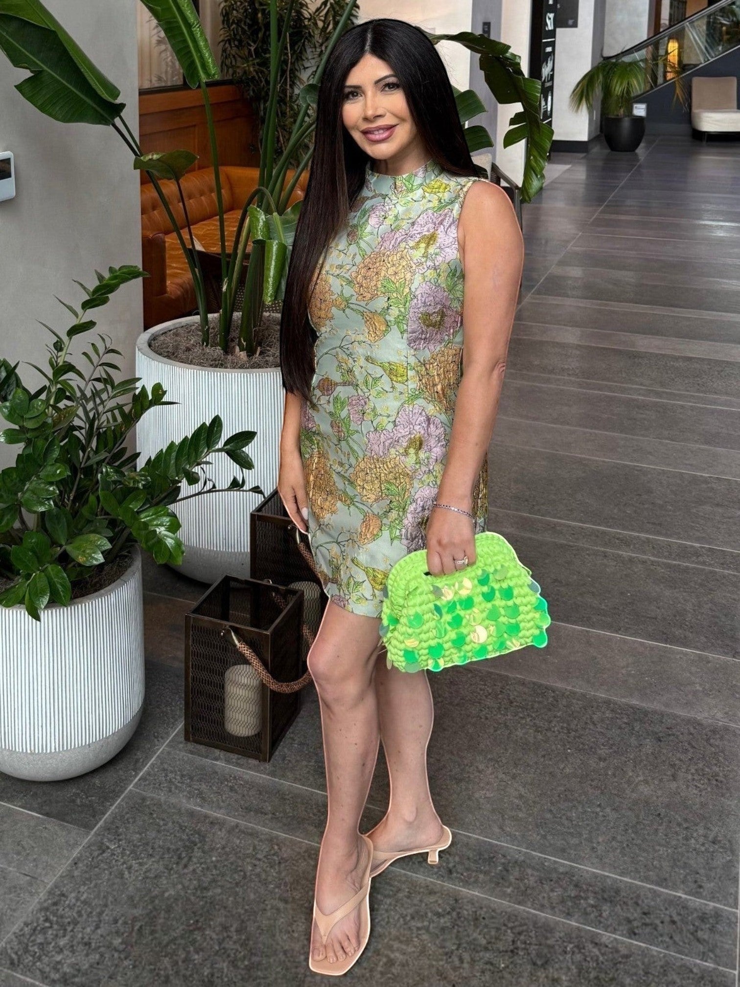 Woman holding a Mialur green woven handbag with iridescent paillettes, styled with a floral dress and sandals.