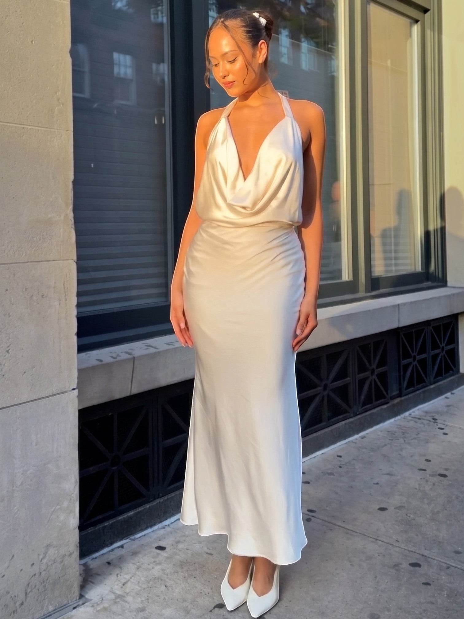 Mialur Kameron champagne satin maxi dress with a draped cowl neckline and halter straps worn by a model outdoors.
