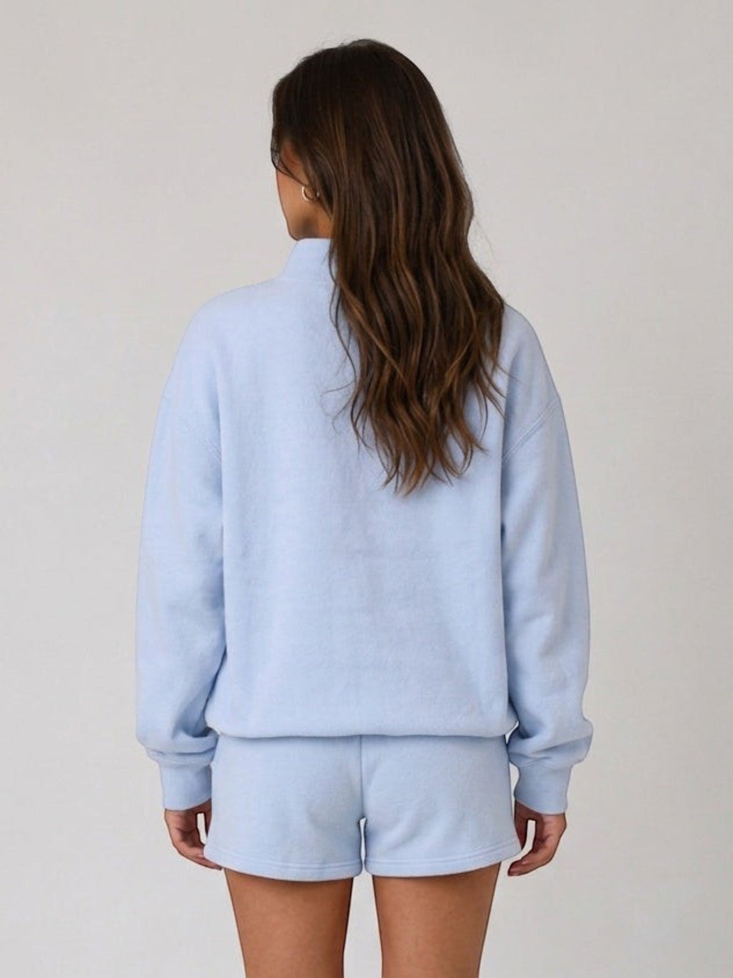 Back view of a woman wearing a Mialur light blue mock neck sweatshirt and matching shorts set.