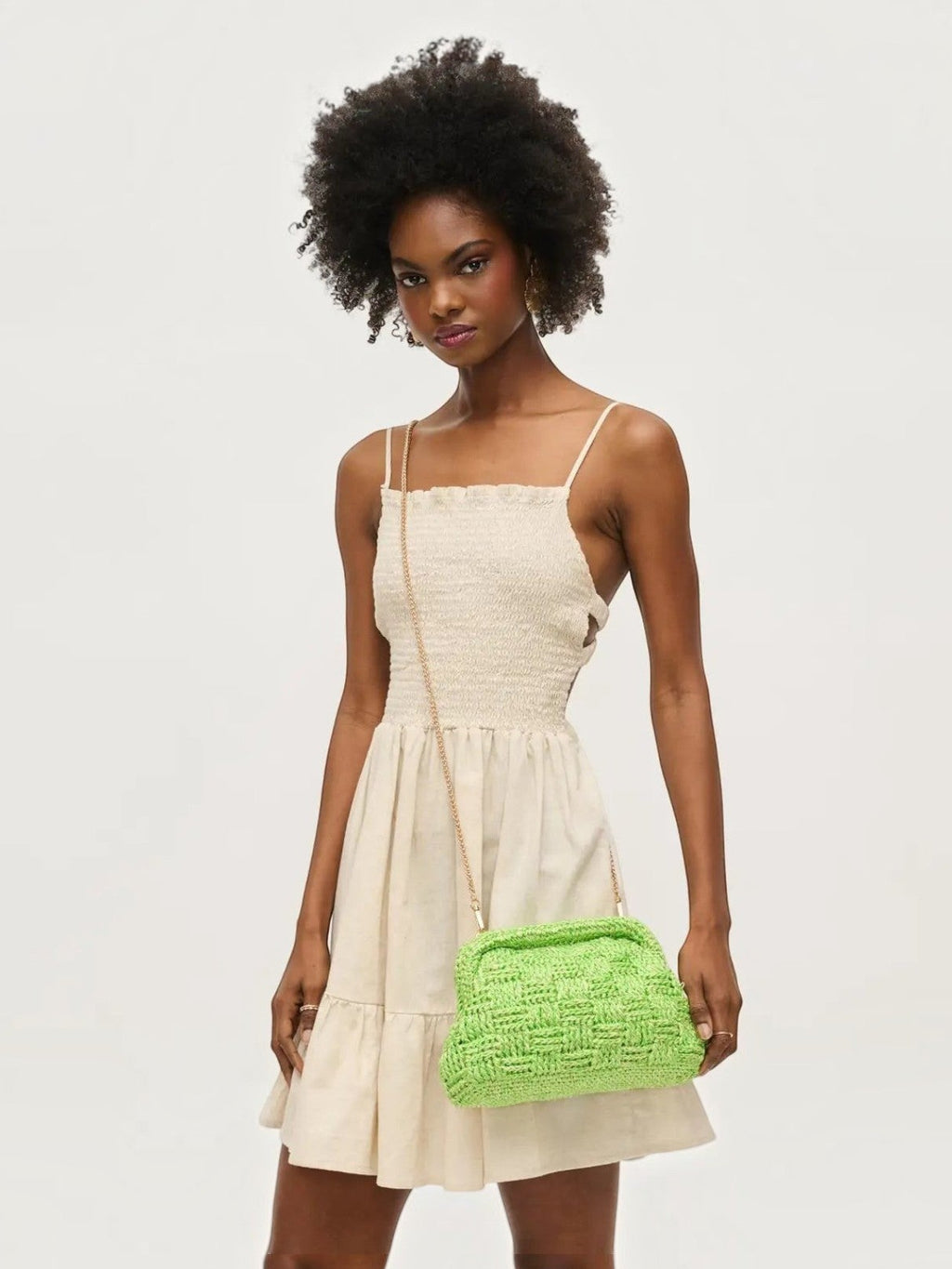 Model wearing a Mialur lime green woven clutch with a gold chain strap and a beige summer dress.