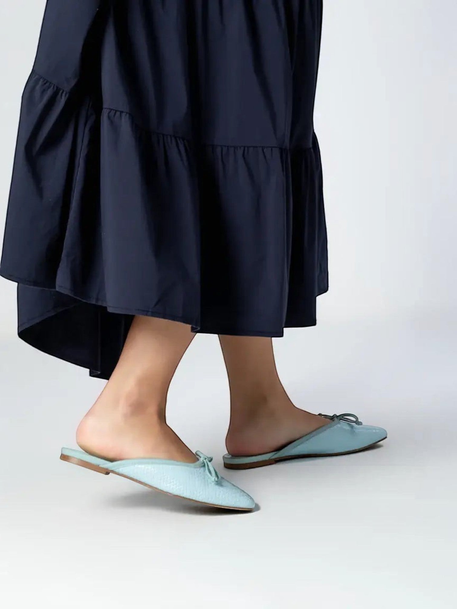 Mialur mint green faux snake leather flats with a delicate bow detail worn with a navy midi skirt on a white background