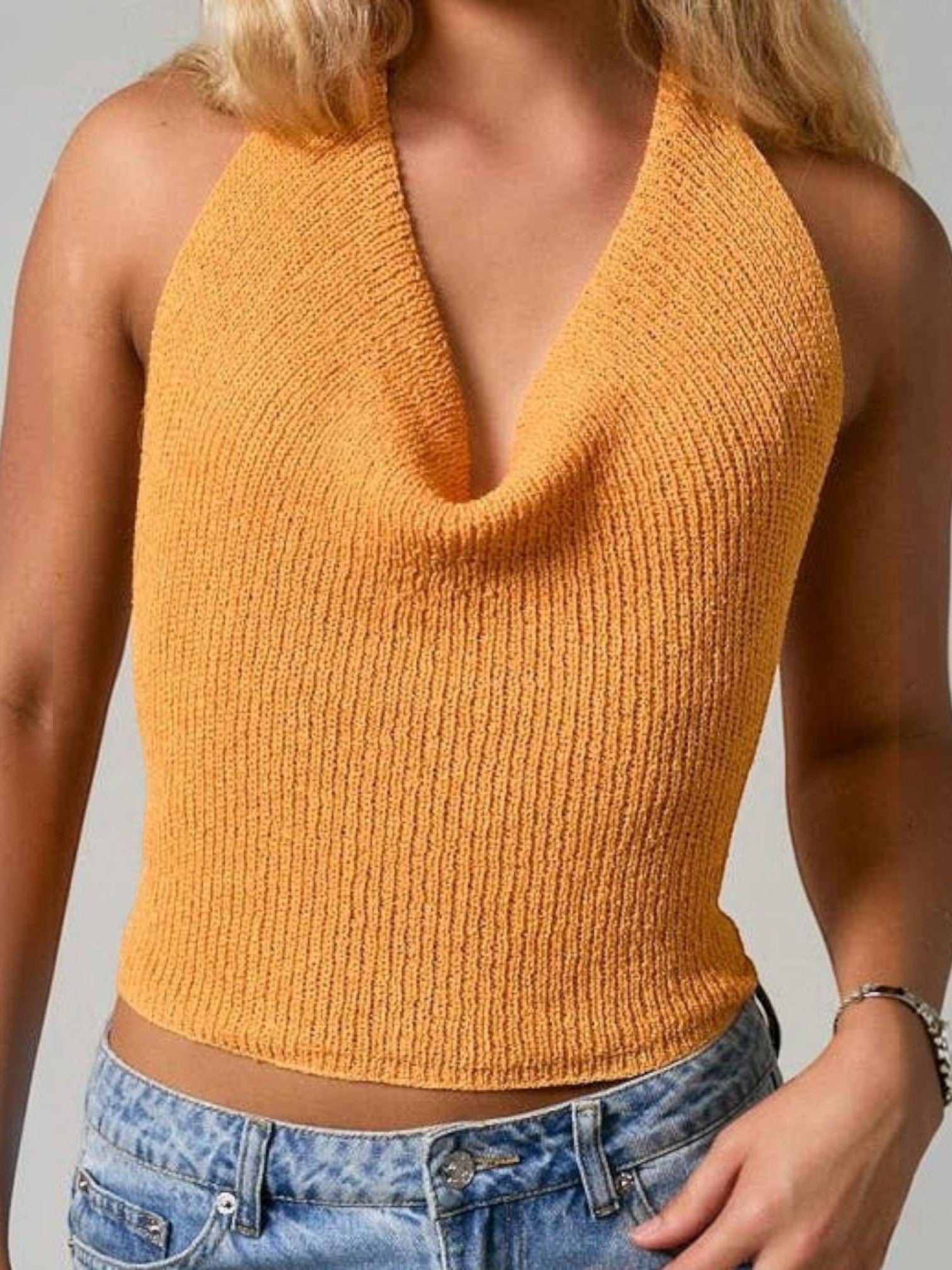 Mialur orange knit halter top with a draped cowl neckline and open-back design worn with denim jeans.