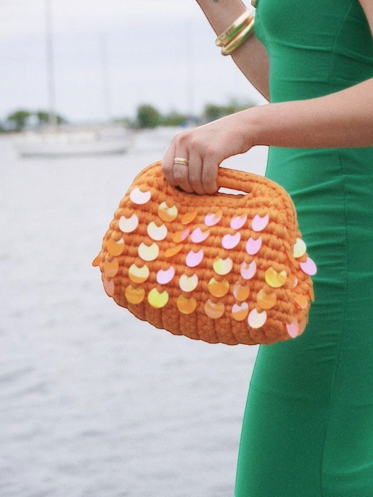 Mialur vibrant orange knit clutch bag featuring colorful iridescent sequins held by a woman in a green dress