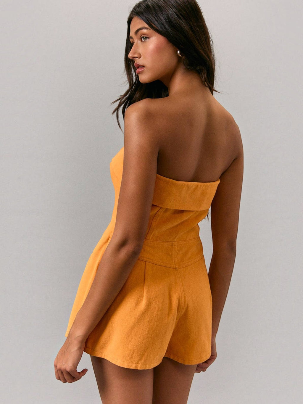 Model wearing a Mialur orange strapless cotton romper with a fitted silhouette and built-in shorts, side view.