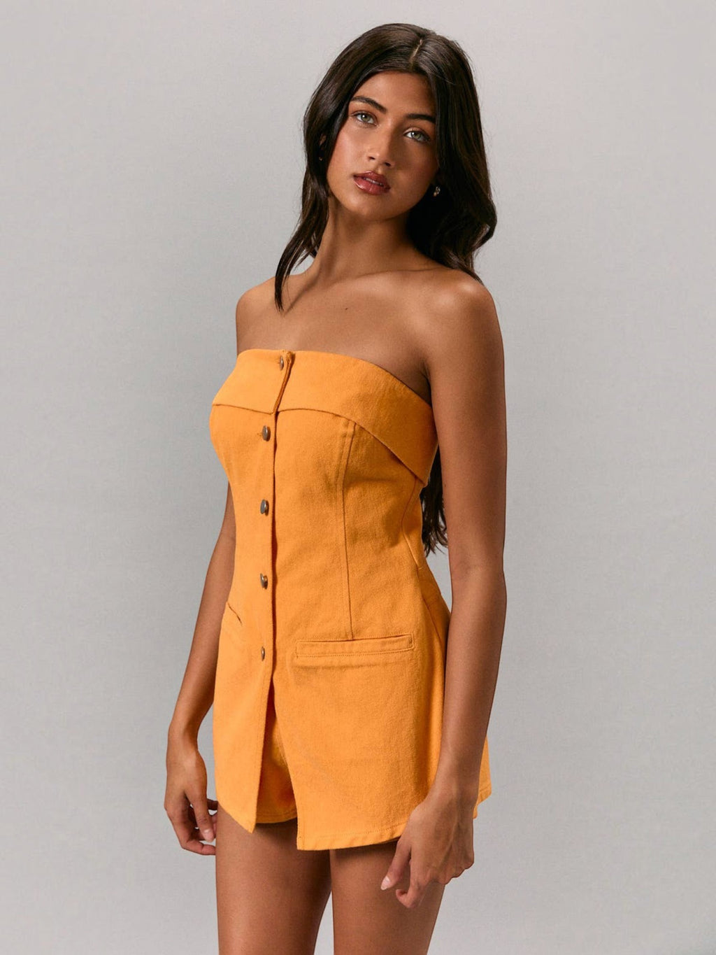Model wearing a Mialur orange strapless cotton romper with front button closure and patch pockets