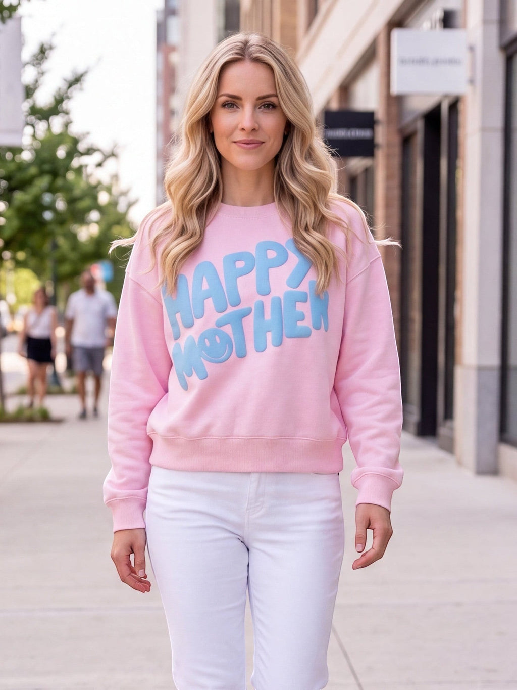 A woman wearing a Mialur pink Happy Mom Mock Top with blue HAPPY MOTHER graphic and smiley face, paired with white jeans.