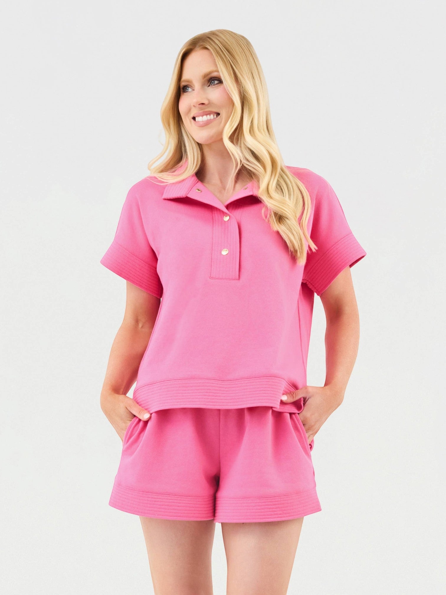 Model wearing Mialur pink two-piece set with collared short-sleeve top, gold buttons, and matching drawstring shorts.