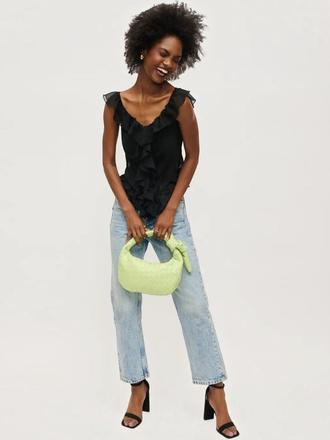 Mialur pistachio green vegan leather woven knot clutch held by a smiling woman in a black ruffled top and jeans.