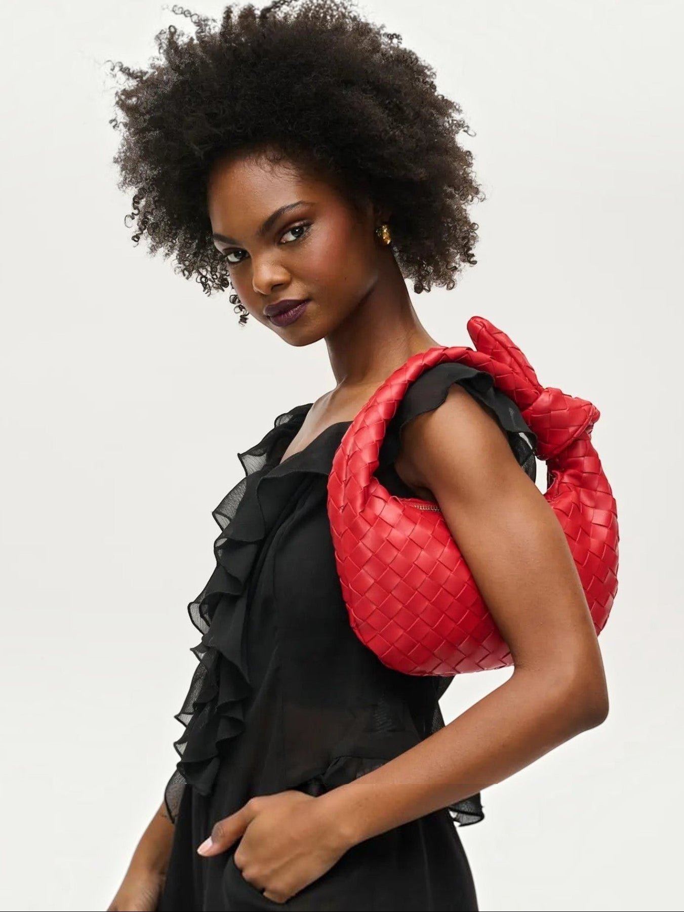 Mialur Ruby Luxe Knot Clutch in ruby red woven vegan leather with a signature knot handle held by a model.