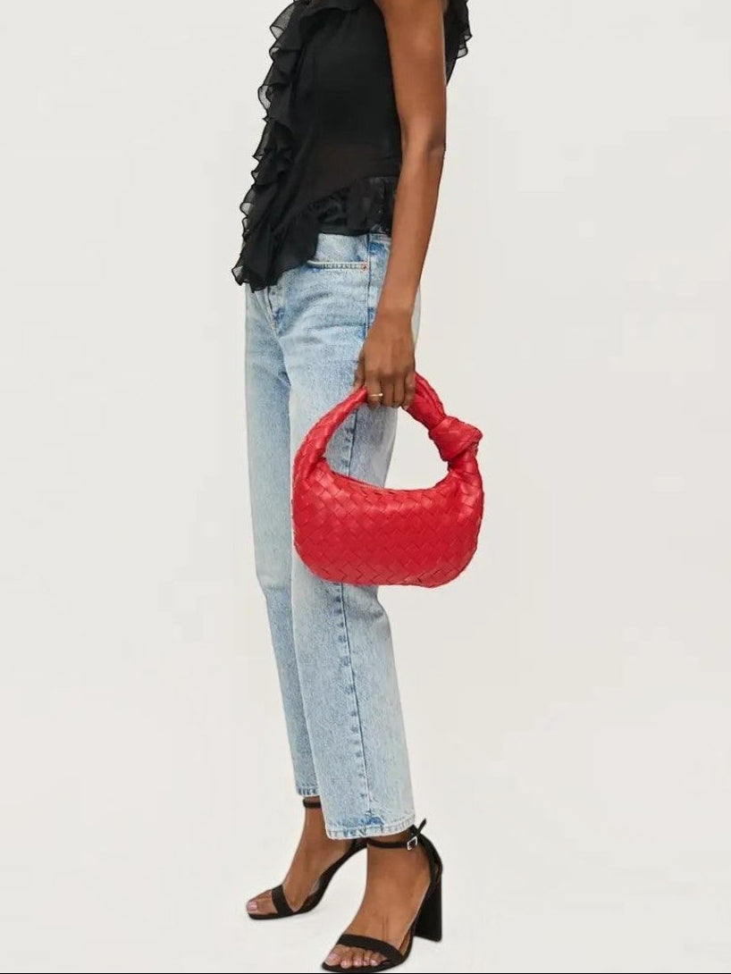 Model wearing a black ruffled top and jeans holding a Mialur ruby red woven vegan leather knot clutch handbag