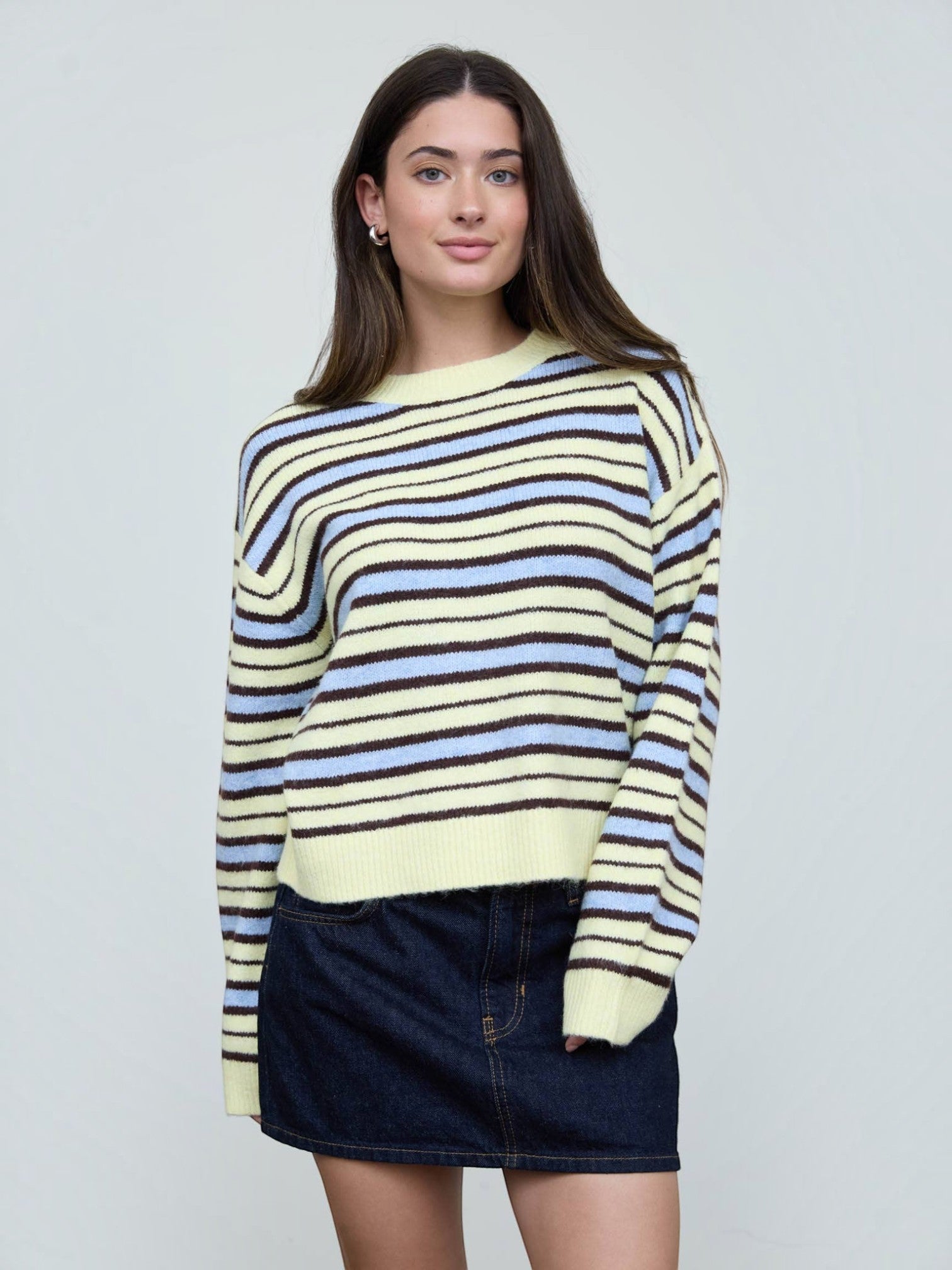 Mialur model wearing a relaxed-fit cream, light blue, and brown striped crew neck knit sweater with ribbed cuffs.