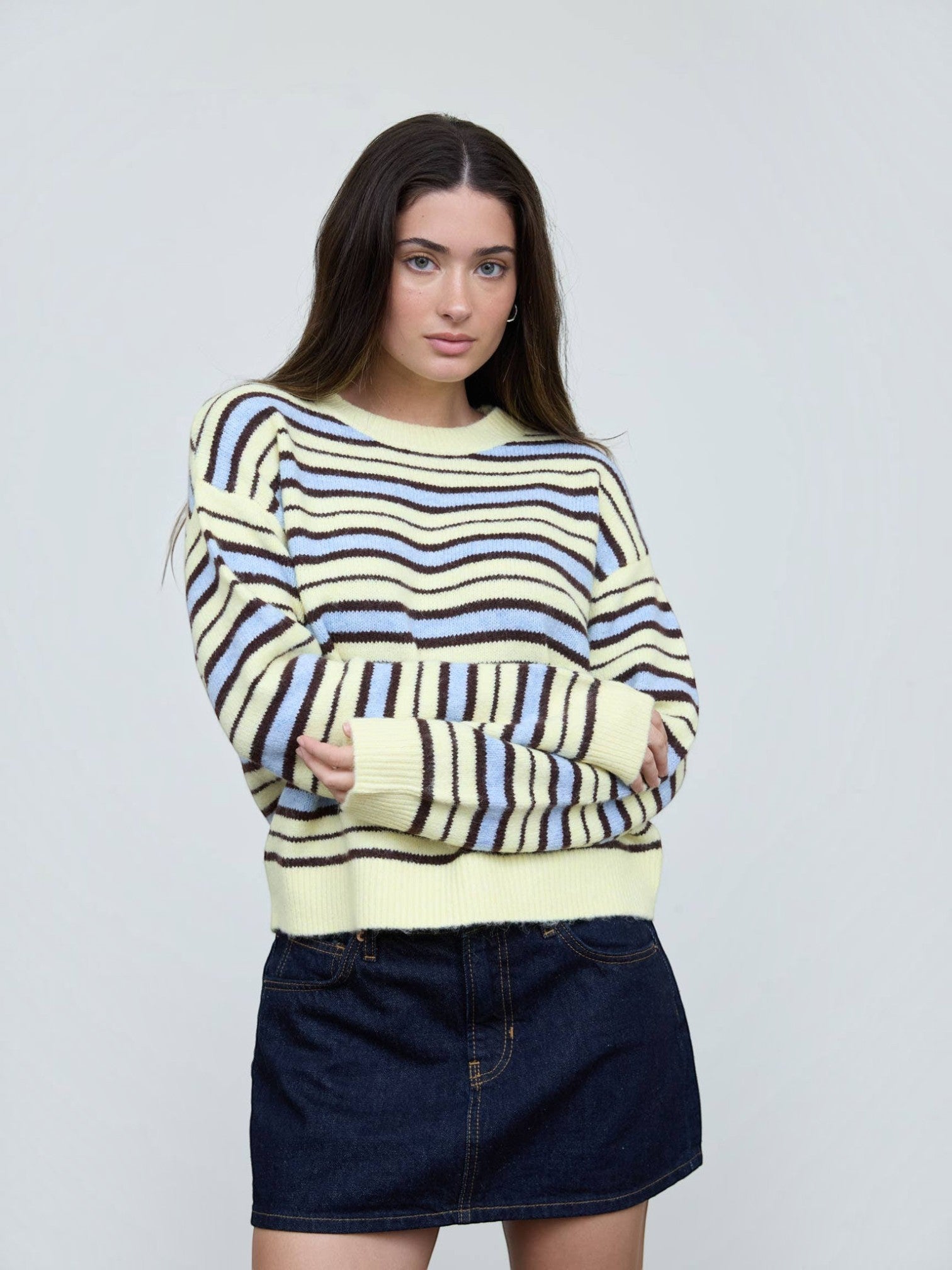 Mialur model wearing a relaxed fit cream, light blue, and brown striped crew neck knit sweater with a denim skirt.