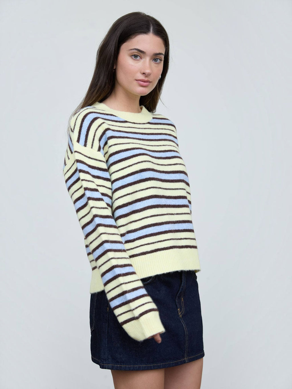 Mialur model wearing a relaxed fit cream, light blue, and brown striped crew neck knit sweater with long sleeves.