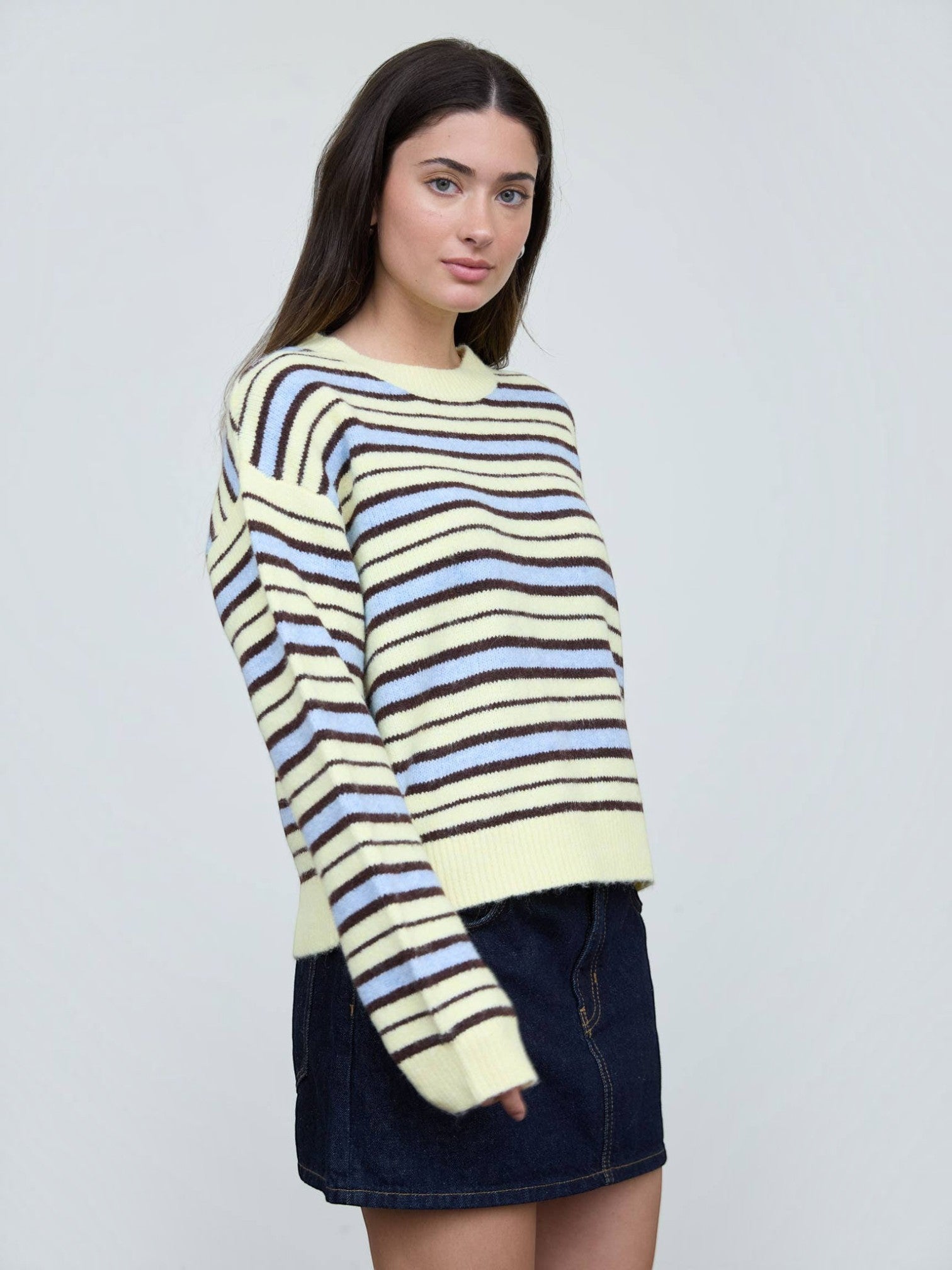 Mialur model wearing a relaxed fit cream, light blue, and brown striped crew neck knit sweater with long sleeves.