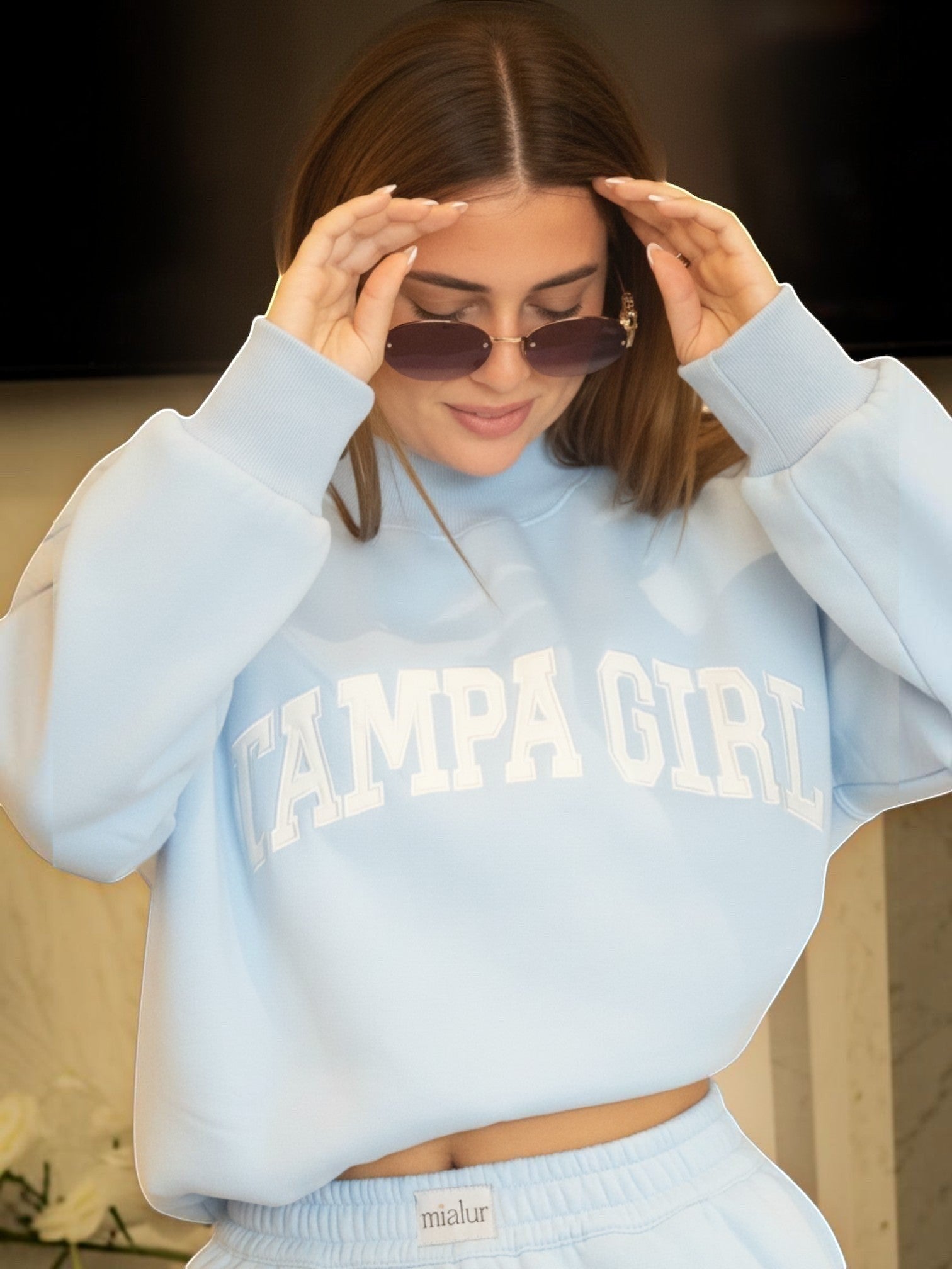 Mialur light blue mock neck sweatshirt with TAMPA GIRL lettering worn by a woman with sunglasses