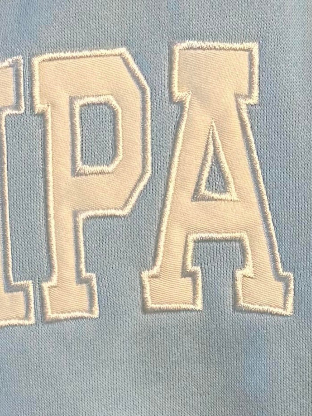 Close-up of Mialur light blue fabric with white embroidered TAMPA GIRL lettering on a mock neck sweatshirt