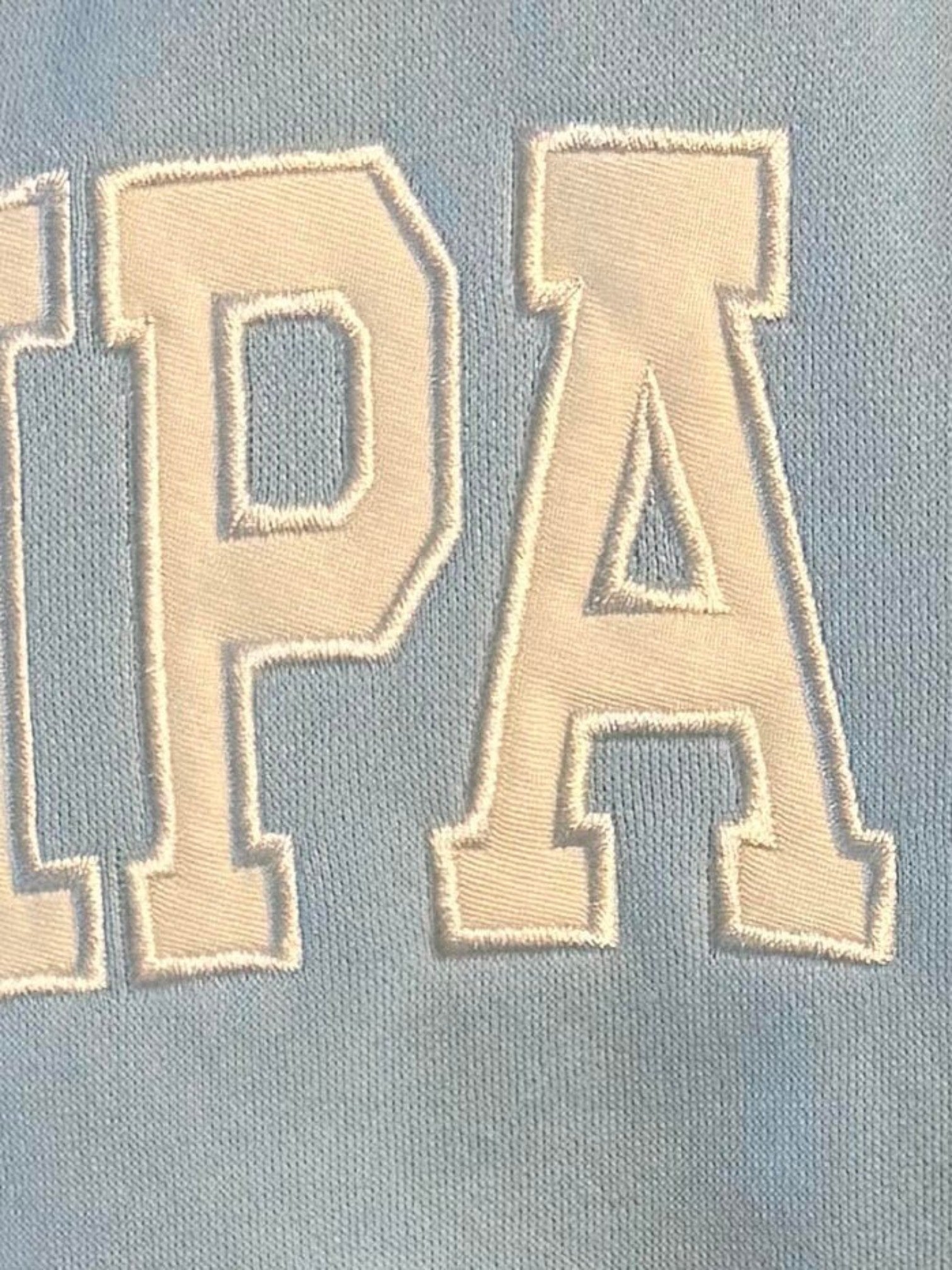 Close-up of Mialur light blue fabric with white embroidered TAMPA GIRL lettering on a mock neck sweatshirt