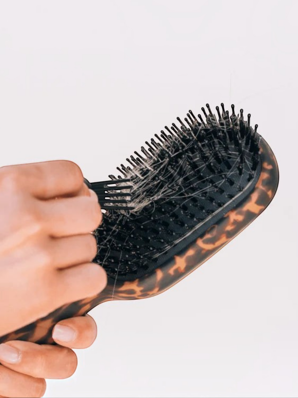 Mialur TELETIES tortoise boar bristle hair brush with a hand using the built-in gold pick to remove hair