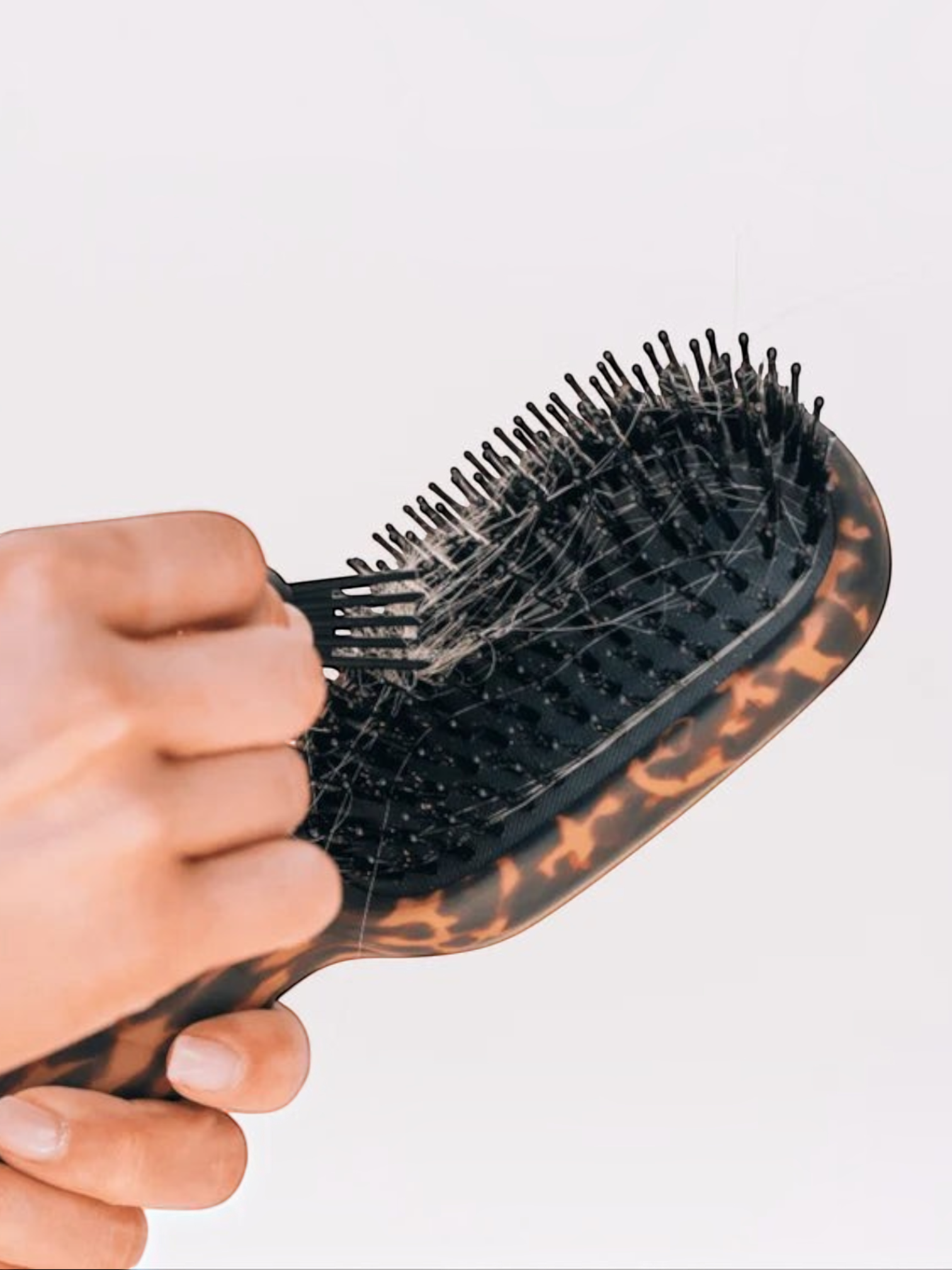 Mialur TELETIES tortoise boar bristle hair brush with a hand using the built-in gold pick to remove hair