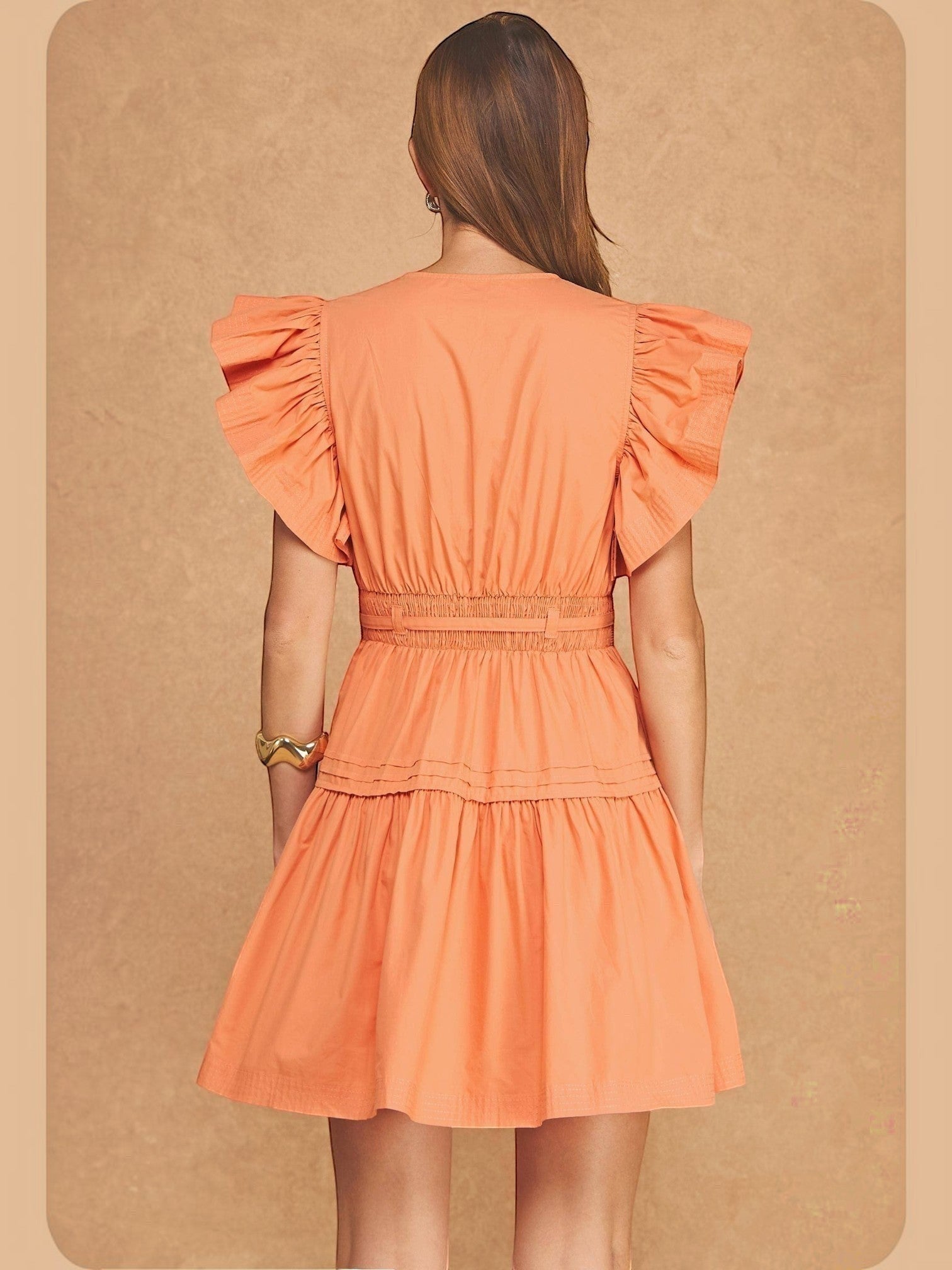 Back view of a model wearing the Mialur Valencia babydoll dress in cantaloupe orange with flutter sleeves and smocked waist
