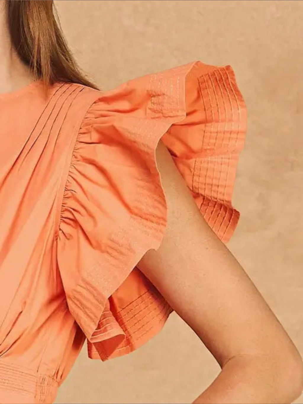 Close-up of Mialur Valencia dress in cantaloupe orange featuring flutter sleeves with delicate ruffle detailing.
