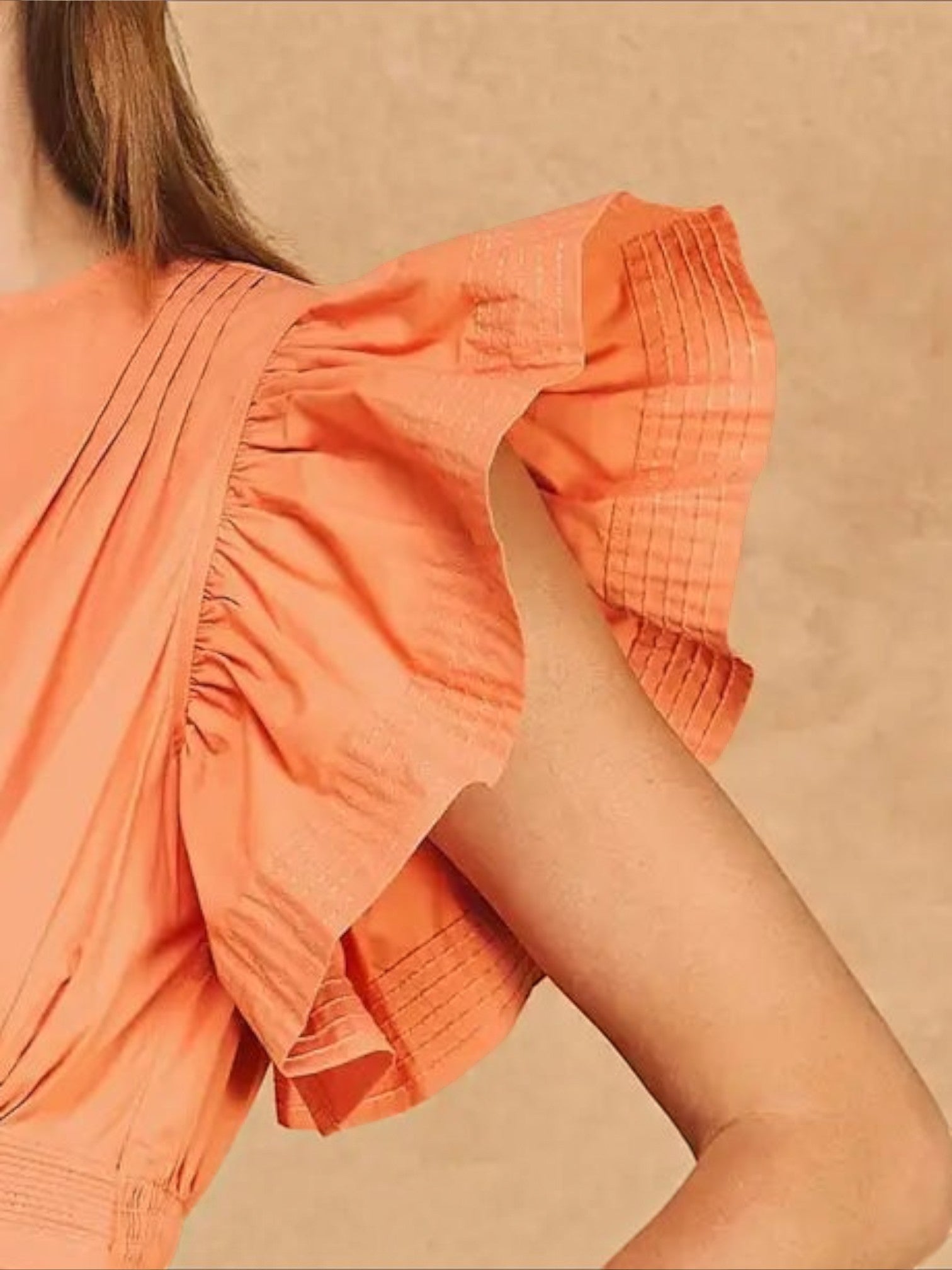 Close-up of Mialur Valencia dress in cantaloupe orange featuring flutter sleeves with delicate ruffle detailing.